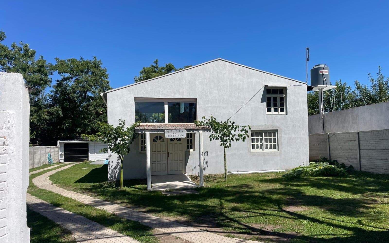Frente de la casa visto desde el parque, con el camino de entrada y el césped